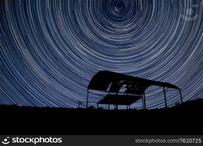 Digital composite image of star trails around Polaris with Beautiful landscape image of old derelict barn silhouette
