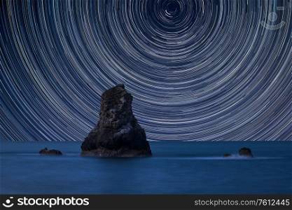Digital composite image of star trails around Polaris with Beautiful long exposure peaceful landscape of rocks in sea