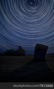 Digital composite image of star trails around Polaris with Beautiful Summer landscape of Neolithic standing stones in English countryside