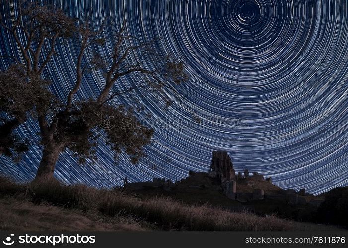 Digital composite image of star trails around Polaris with Medieval castle ruin landscape