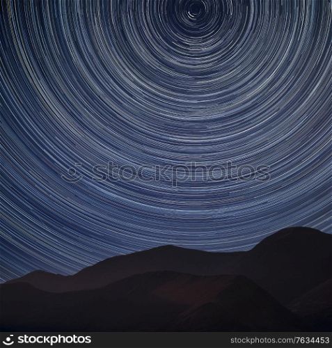 Digital composite image of star trails around Polaris with Stunning landscape image of mountain side in Lake District