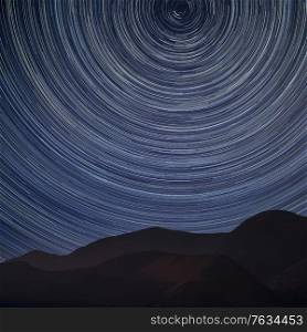 Digital composite image of star trails around Polaris with Stunning landscape image of mountain side in Lake District
