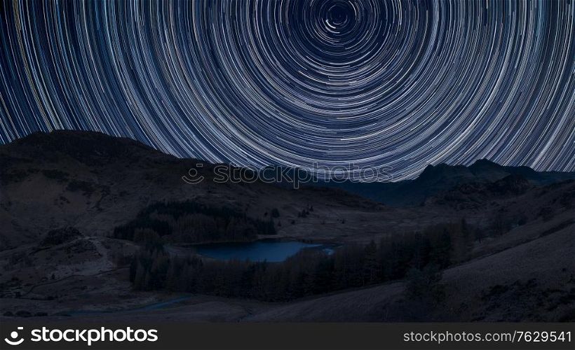 Digital composite image of star trails around Polaris with Stunning sunrise landscape image of Blea Tarn in UK Lake District
