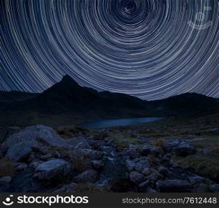 Digital composite image of star trails around Polaris with Stunning vibrant Beautiful landscape image of stream near Llyn Ogwen in Snowdonia with Tryfan