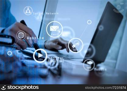 Digital marketing media (website ad, email, social network, SEO, video, mobile app) in virtual screen.designer hand working with stylus on smart phone and digital tablet and laptop on wooden desk in office.