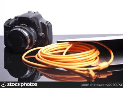 Digital photo camera connected to laptop with orange rolled cable.. Digital photo camera connected to laptop with orange rolled cable
