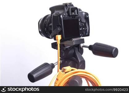 Digital photo camera on black tripod with orange rolled cable isolated on white background.. Digital photo camera on black tripod with orange rolled cable