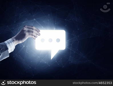 Digital speech icon. Hand of businessman holding glowing speech icon on dark background