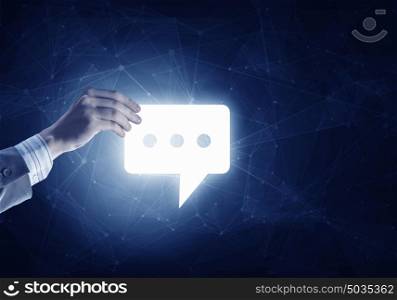 Digital speech icon. Hand of businessman holding glowing speech icon on dark background