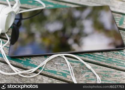 digital tablet and headphones on wooden table, outdoor