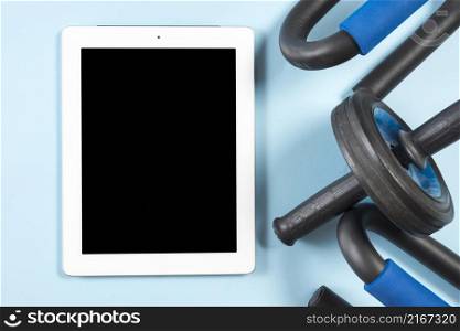 digital tablet with black display gym equipments blue backdrop