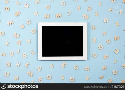 digital tablet with black screen display surrounded with wooden letters blue background