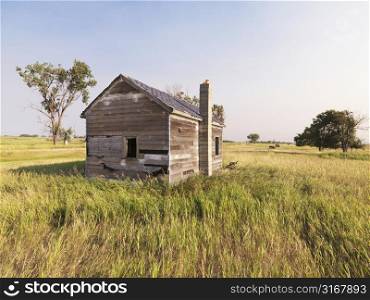 Dilapidated wooden house in rural field.