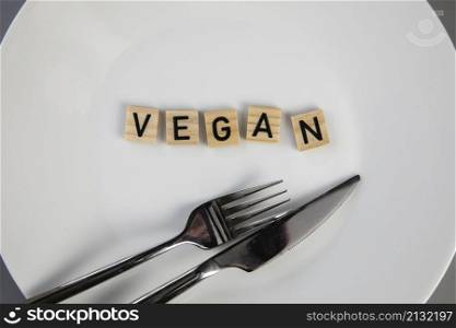 Dining plate with fork and knife with the text VEGAN, concept of dieting vs healthy veganism,vegetarian and healthy lifestyle top view background. Dining plate with fork and knife with the text VEGAN, concept of dieting vs healthy veganism,vegetarian and healthy lifestyle top view