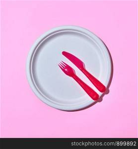 Dining set of plastic colored tableware on a light pink background with copy space. Top view.. Served place with disposable plastic utensils on pink.