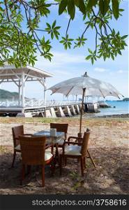 Dining Table and umbrella. Under a tree in a seaside restaurant. Cloudy atmosphere.