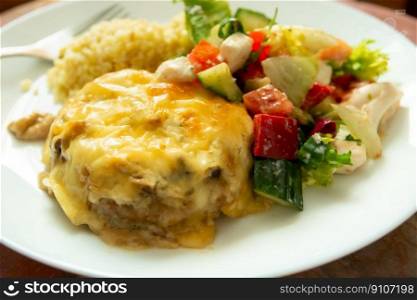 Dinner dish with large minced cutlet with yellow cheese and salad with red peppers, cucumber and white cheese.