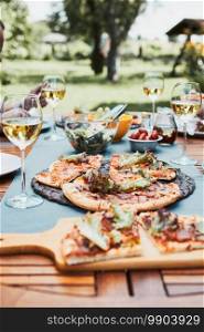 Dinner in a home garden. Pizza, salads, fruits and white wine on table in a orchard in a backyard. Dinner in a home garden. Pizza, salads, fruits and white wine on table in a backyard