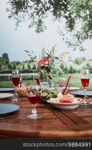 Dinner in an apple orchard garden on wooden table with salads and wine decorated with flowers. Close up of table with food prepared for family dinner