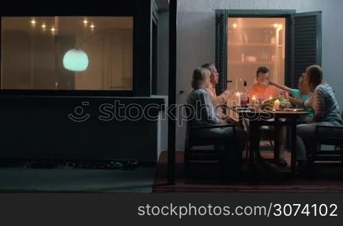 Dinner of a big family. Grandparents, parents and child going to meal on outdoor terrace by the house with lit candles on the table. Mother comforting crying child