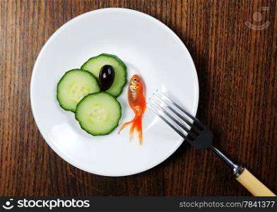dinner setting on wooden table. fork and plate with golfish and salad