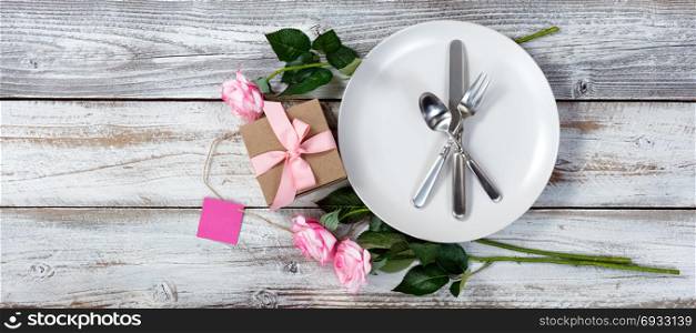 Dinner setting with pink roses and gift box on rustic white wood in flat lay view