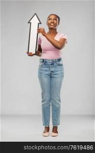 direction and people concept - happy african american young woman holding big white thick upwards arrow over grey background. african woman with upwards arrow