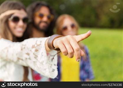 direction, gesture and people concept - hippie woman with friends pointing finger outdoors. happy hippie woman pointing finger outdoors