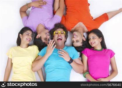 Directly above shot of cheerful friends sharing secret while lying over white background
