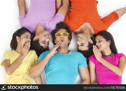 Directly above shot of friends sharing secret while lying over white background