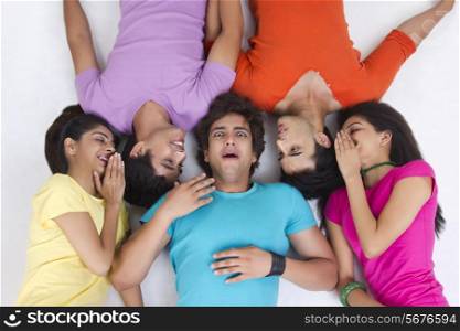 Directly above shot of friends whispering while lying over white background