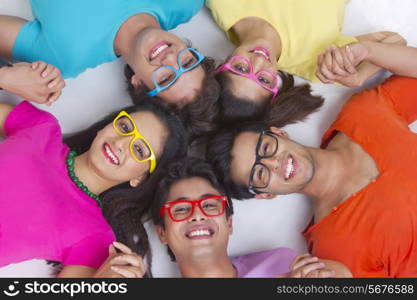 Directly above shot of trendy friends holding hands while lying in circle on white background