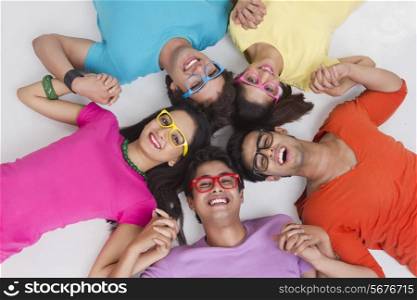 Directly above shot of trendy friends holding hands while lying in circle on white background