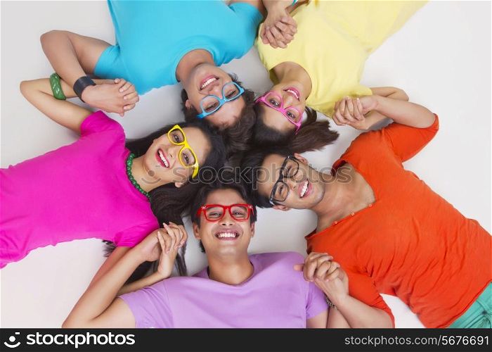 Directly above shot of young friends holding hands while lying in circle on white background
