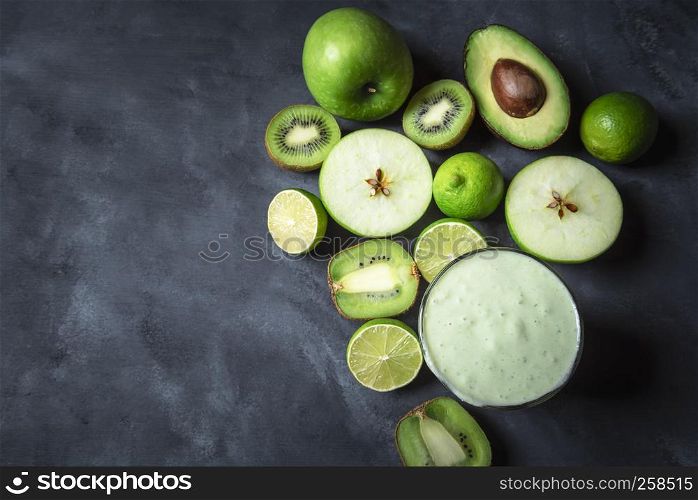 Directly above view of a glass of smoothie surrounded by green fruits, on a dark grey kitchen table. Healthy breakfast. Detox context. Dieting food.