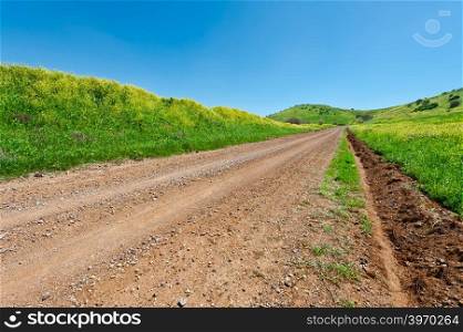 Dirt Road between Green Fields of the Golan Heights in Israel