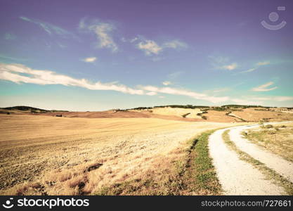 Dirt road between the plowed fields and the hills of Tuscany in Italy. Vintage style