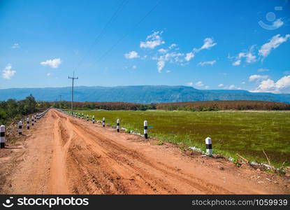 Dirt road gravel in agriculture countryside go to the mountain blue sky background