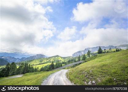 Dirt road in a mountain landscape with green meadows and a blue sky