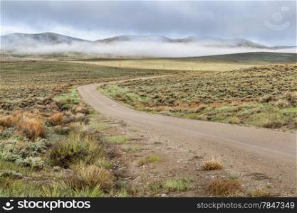 dirt road in a mountain valley with hills covered by sagebrush in early spring morning, North Park, Colorado
