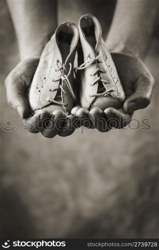 Dirty hands holding a pair of baby shoes. Very shallow depth of field.