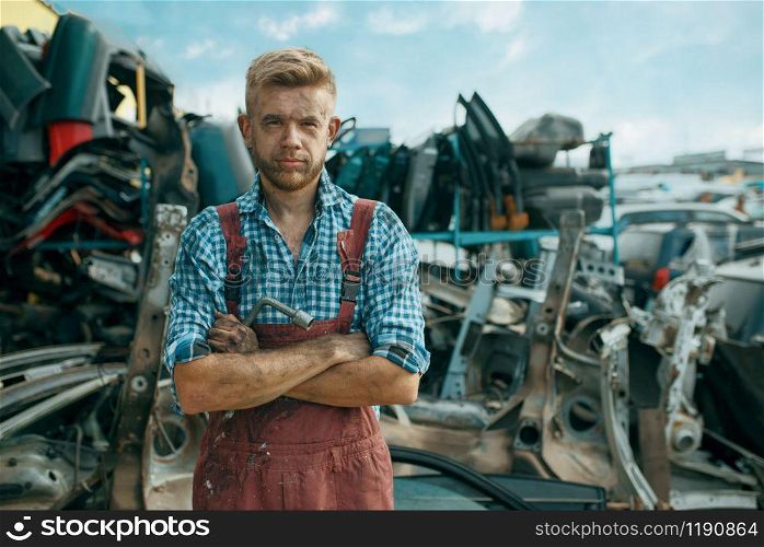 Dirty male repairman on car junkyard. Auto scrap, vehicle junk, automobile garbage, abandoned, damaged and crushed transport