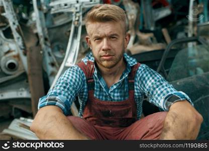 Dirty male repairman with wrench on car junkyard. Auto scrap, vehicle junk, automobile garbage, abandoned, damaged and crushed transport. Dirty male repairman with wrench on car junkyard