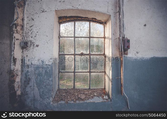 Dirty old window on a grunge wall with cracks and pealing blue paint with an electrical switch beside