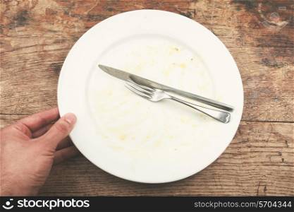 Dirty plate and cutlery with a man&rsquo;s hand next to it