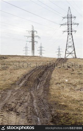 Dirty rustic road with traces from the tractor next to power lines.