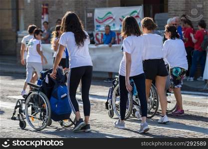 Disabled Athlete in a Sport Wheelchair during Marathon Helped by Female Runners.. Disabled Athlete in a Sport Wheelchair during Marathon Helped by Female Runners