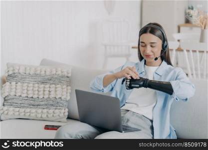 Disabled caucasian young woman in headset has online conference on laptop. Equal rights for handicapped. Remote manager working at home on quarantine. Modern bionic prosthesis technology.. Disabled caucasian young woman in headset has online conference on laptop. Equal rights.