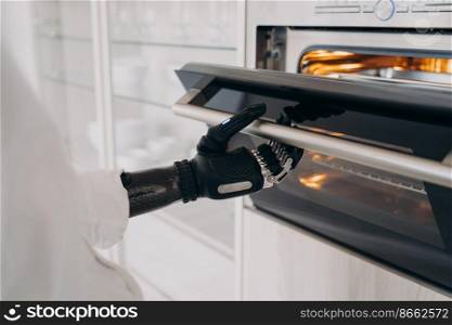 Disabled female holding electric ovens door by bionic prosthetic arm. Person with disability opening or closing oven with artificial hand, preparing dinner, cooking meals using kitchen appliance.. Disabled person opening electric ovens door by bionic prosthetic arm, preparing dinner in kitchen