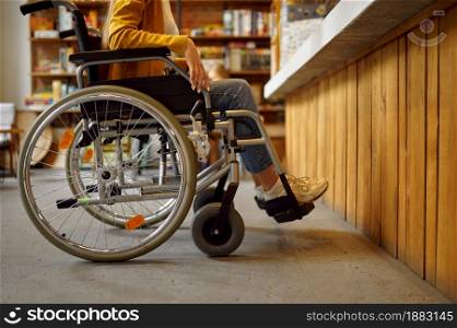 Disabled female student in wheelchair at the counter, disability, bookshelf and university library or cafe interior on background. Handicapped woman in college, paralyzed people get knowledge. Disabled female student in wheelchair at counter